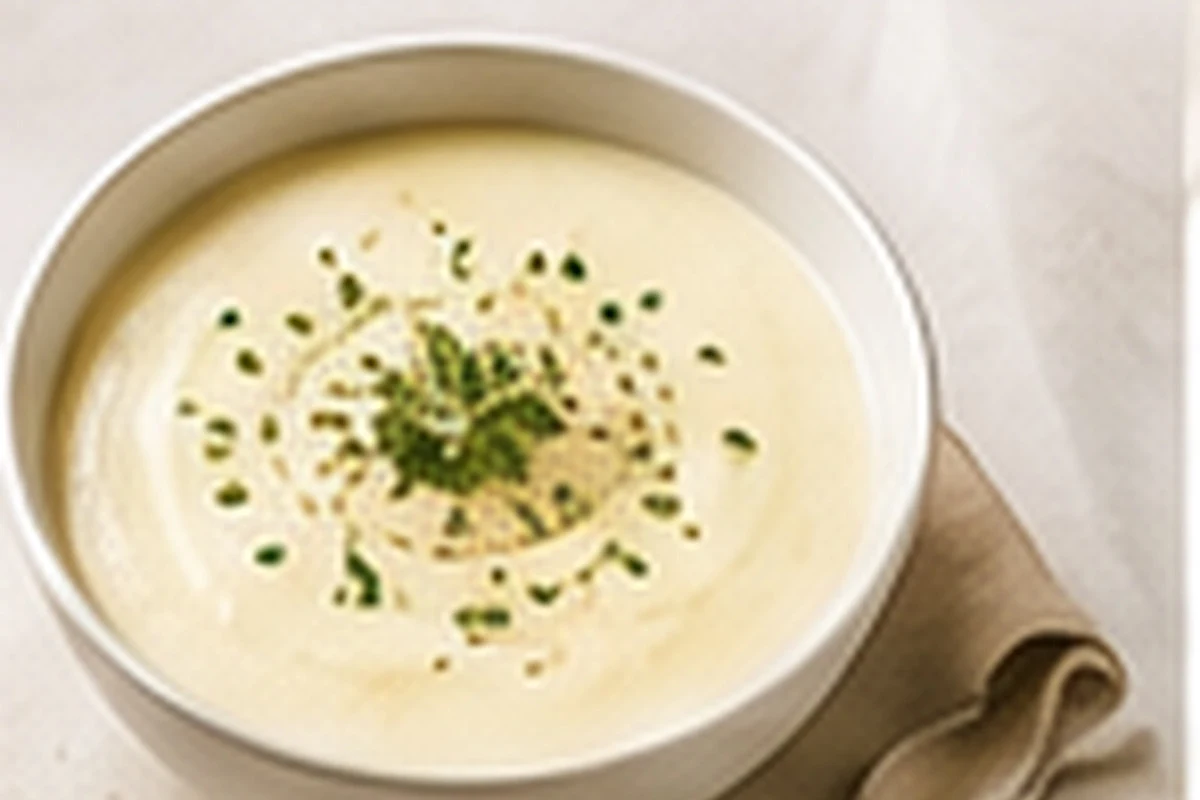 A bowl of smooth pale fennel and potato soup topped with chopped dill.