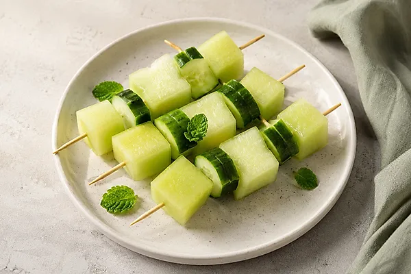 Small skewers with melon cubes and cucumber slices on a light plate.
