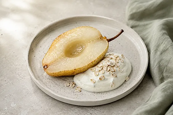 Warm baked pear halves with a spoonful of vanilla quark in a light bowl.
