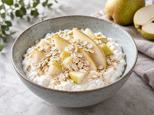 Bowl of creamy low-fat quark topped with steamed pear cubes and oats